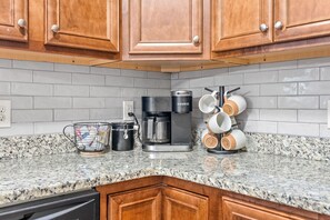 A kitchen with wooden cabinets, a coffee maker, a kettle, and a mug rack. - Fire Pit, Central to RTJ, Downtown Auburn & Opelika - Sleeps 12 (Opelika)