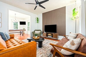 A modern living room with a sofa, armchair, coffee table, and a flat-screen TV on a wooden stand.