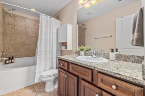 A modern bathroom with a bathtub, toilet, and sink. - Fire Pit, Central to RTJ, Downtown Auburn & Opelika - Sleeps 12 (Opelika)