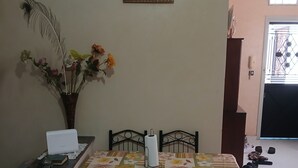 Un comedor con una mesa cubierta por un mantel floral, rodeada de cuatro sillas. Un jarrón con flores está sobre la mesa, y un cuadro enmarcado cuelga de la pared de arriba.