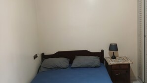Un dormitorio con cama, almohadas, una mesita de noche con lámpara y un armario.