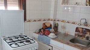 Uma cozinha com armários brancos, fogão, pia e janela com persianas.