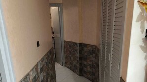 Un pasillo estrecho con piso de baldosas, una puerta al final y una pared con diseño de piedra.