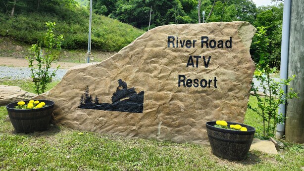 Suuri kivitaulu, jossa lukee ”River Road ATV Resort” ja on kuvattuna mönkijän ajajan siluetti.