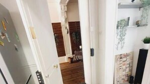 Een smalle keuken met een koelkast, een deur naar een houten kamer en een plank met planten.