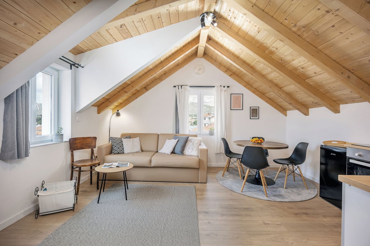 A cozy loft-style room with a high ceiling, a sofa, a dining table, and a kitchen area.