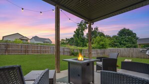An outdoor patio area with a metal fire feature, wicker furniture, and a wooden fence in the background. - Game Room - Patio + Grill - Sleeps 9 - King Bed (Clarksville)