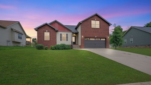 A two-story house with a brick facade, a front garage, and a well-maintained lawn. - Game Room - Patio + Grill - Sleeps 9 - King Bed (Clarksville)