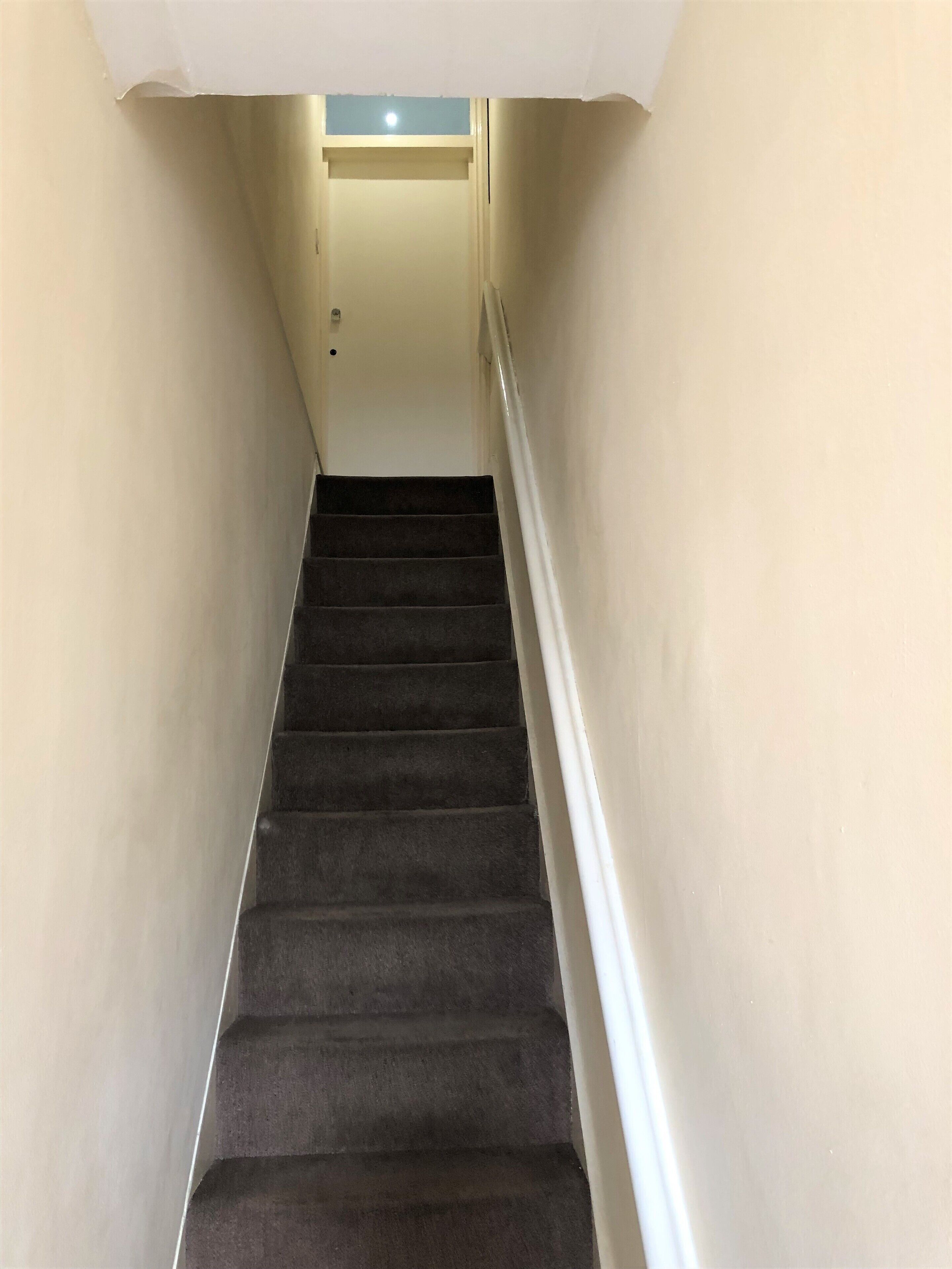 A narrow staircase with carpeted steps and white walls.