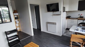A modern kitchen with a built-in oven, a microwave, and a coffee machine. There is a window with blinds, a wooden chair, and a small table. - Studio/cabine "Les Corsaires" (Berck)