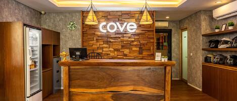 Een houten receptiebalie, een bord met de naam 'cove' en een moderne keuken met apparatuur en planken.