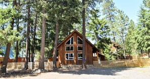 A wooden cabin with a triangular roof, surrounded by tall pine trees.