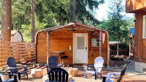 Eine Holzhütte mit einer Tür und einer kleinen Veranda, komplett mit Adirondack-Stühlen und Holzschemeln.