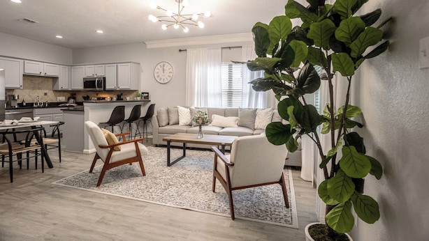 Een moderne keuken met witte kasten, een magnetron, en een eethoek met tafel en stoelen. Er is een woonkamer met een bank en een salontafel.