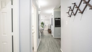 Een gang met een lichtgrijze vloer, witte wanden en een 'Welcome' bord. Achtergrond met houten wandplanken en een plant.
