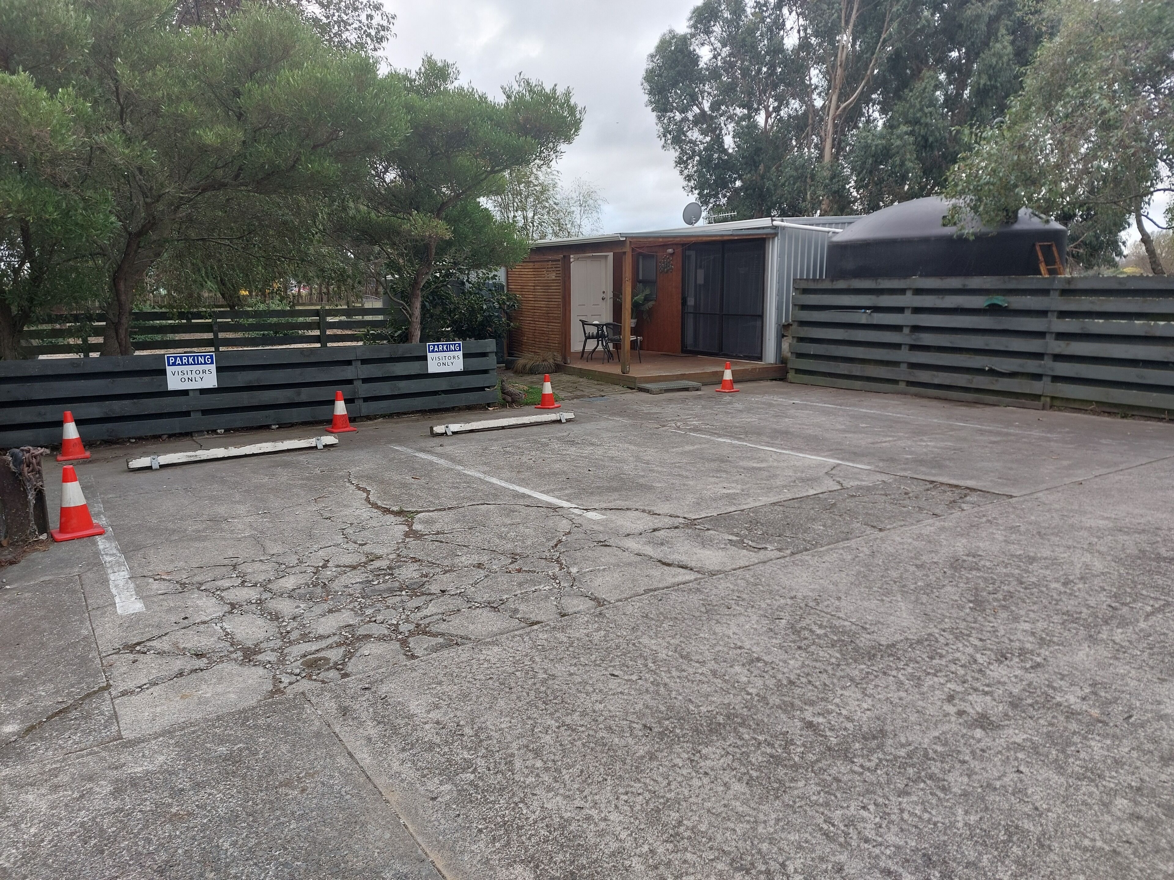 A parking area with visitor signs, a small building, and a fenced area with trees.