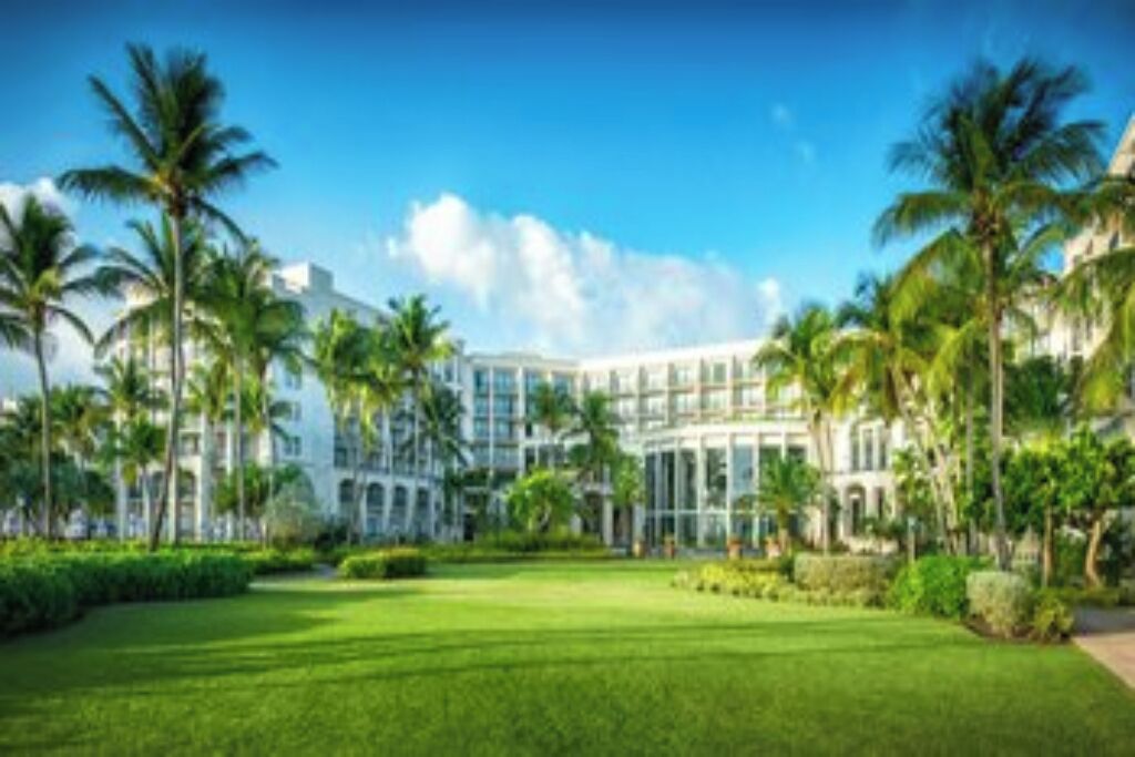 A large, modern hotel with a symmetrical facade, surrounded by well-maintained lawns and palm trees.