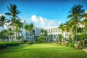 Een groot, modern hotel met een symmetrische gevel, omgeven door verzorgde gazons en palmbomen.