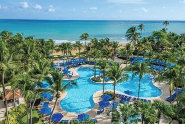 Een resort met een groot centraal zwembad, omringd door palmbomen en ligbedden.