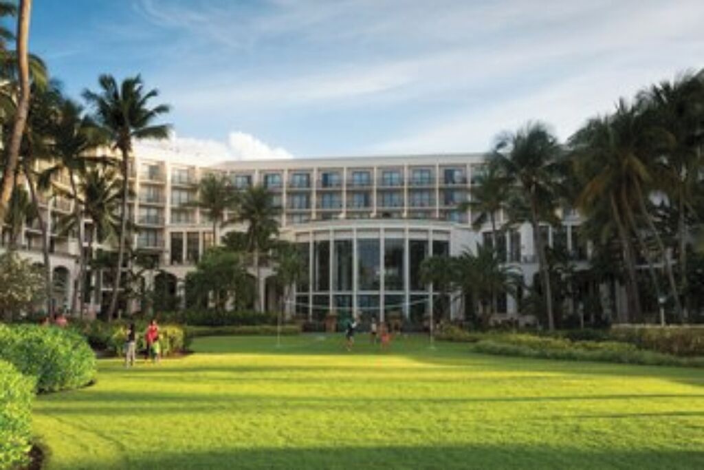 A hotel with a large, modern building, a well-maintained lawn, and palm trees.