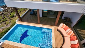 Moderni ulkouima-allasalue, jossa on lasikaide, aurinkotuoleja ja näkymä merelle.