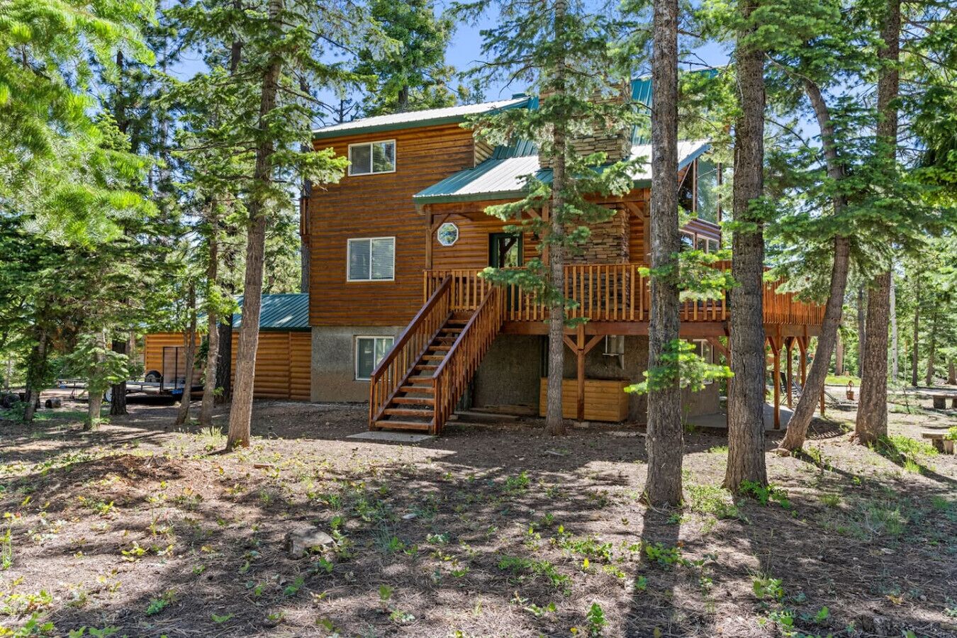 Une cabane avec une façade en bois, un escalier menant à une terrasse, et une forêt environnante.