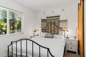 A bedroom with a bed, bedside tables, a wall hanging, and a window with blinds.
