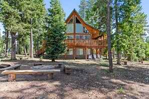 A cabin with a large deck, surrounded by trees.