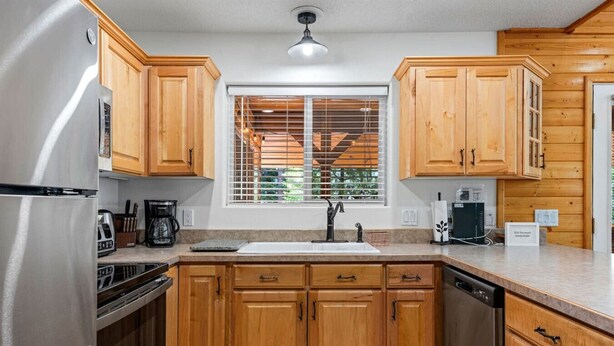 Una cocina con armarios de madera, un refrigerador de acero inoxidable, un lavamanos y una ventana con persianas.