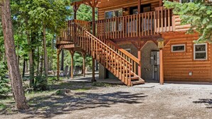 Una cabaña de madera con una escalera de madera que lleva a un balcón, rodeada de árboles.