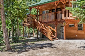 A wooden cabin with a wooden staircase leading to a balcony, surrounded by trees.