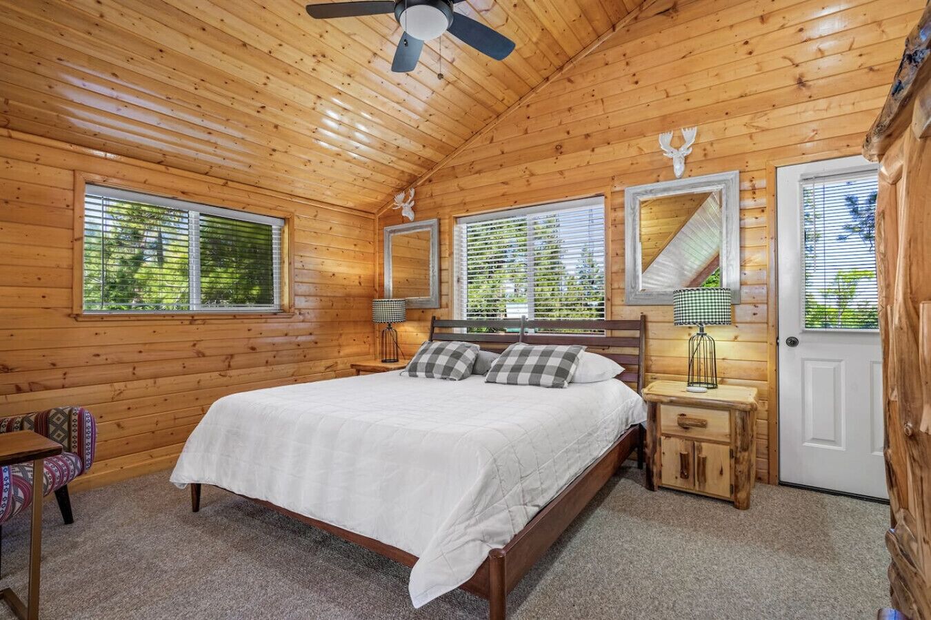 Un dormitorio tipo cabaña de madera con cama, mesitas de noche y ventilador de techo.