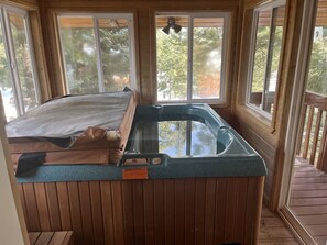 Un jacuzzi en una cabaña de madera con ventanas grandes y una terraza de madera.