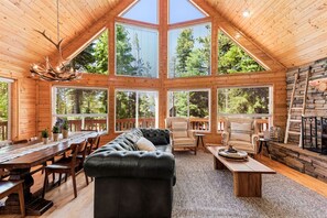 A log cabin interior with a large dining table, two sofas, and a fireplace.