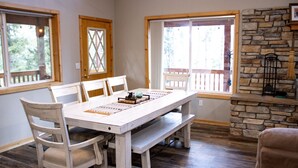 A dining area with a white table and chairs, a wooden bench, and a stone fireplace.