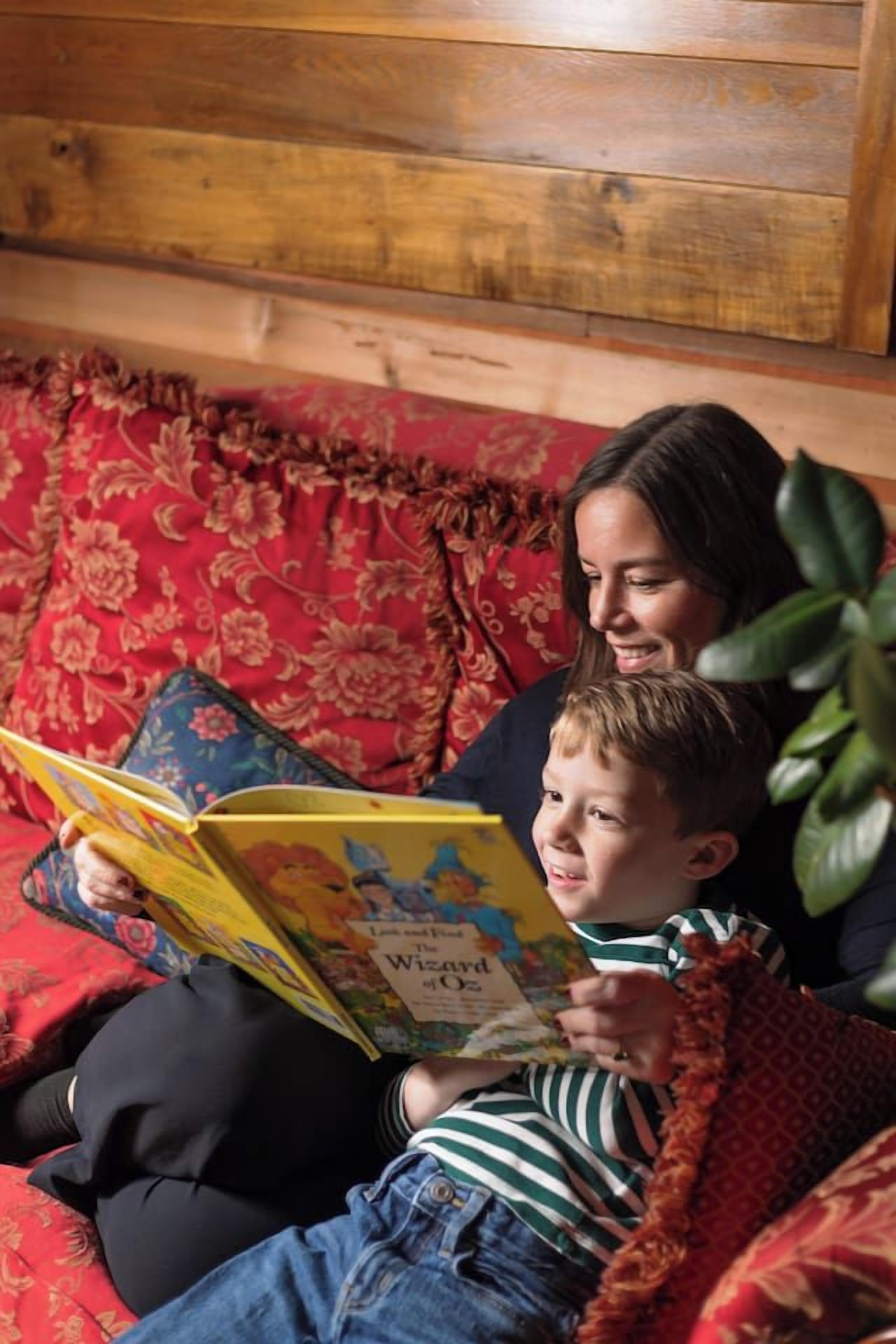 Une personne est assise sur un canapé et lit un livre dont la couverture est ornée de motifs floraux.