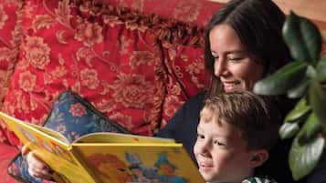 Une personne est assise sur un canapé et lit un livre dont la couverture est ornée de motifs floraux.