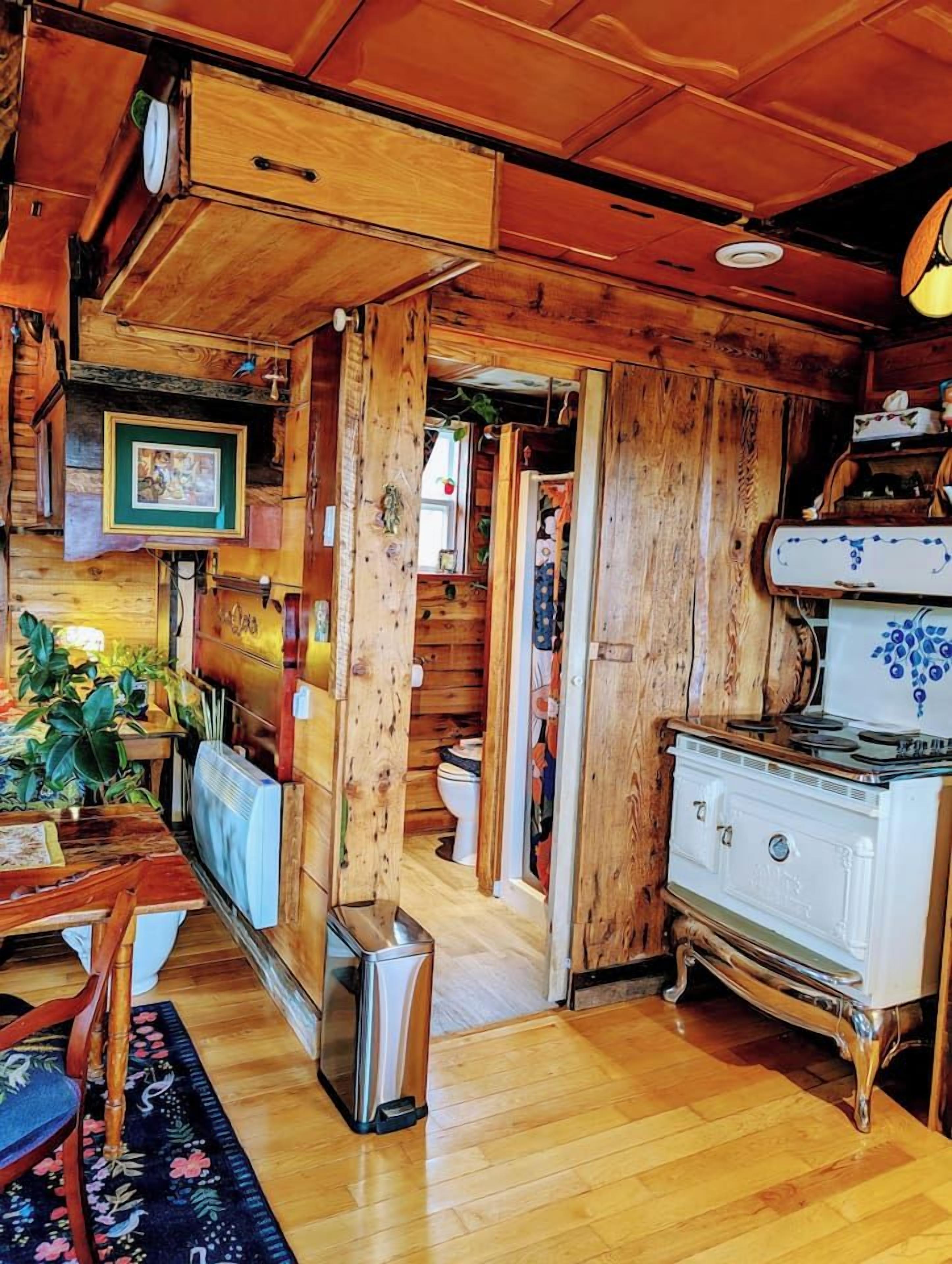 A rustic wooden interior with a dining area, a vintage stove, and a visible bathroom.