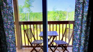 A wooden deck with two folding chairs and a table, overlooking a forested area. - Miracles on Polly - Memory Lane Cabin (Belfast)
