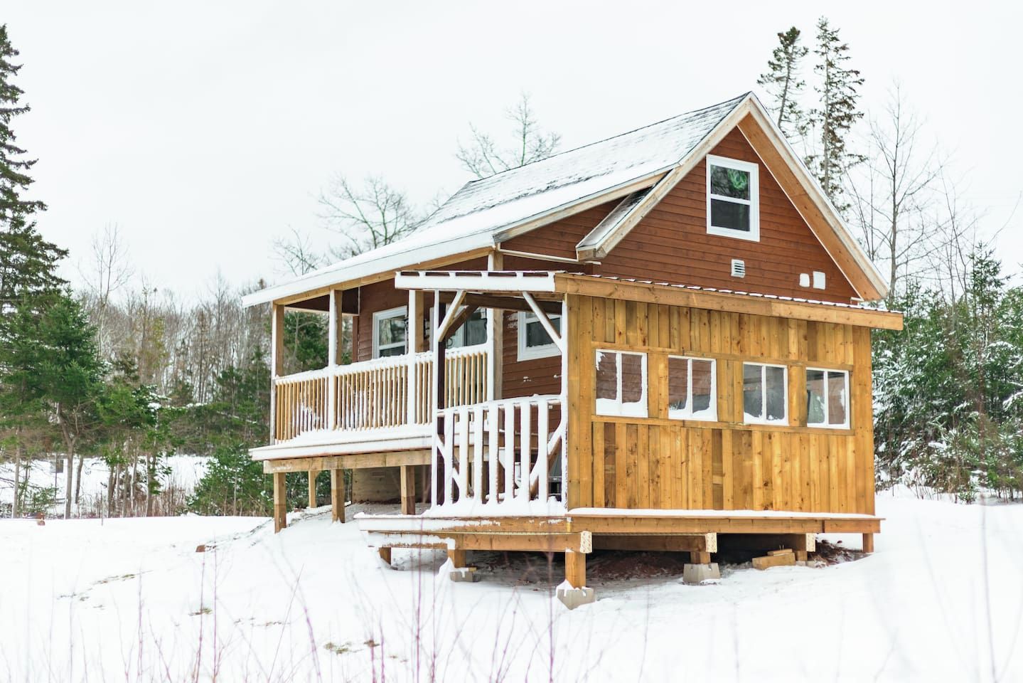 A wooden cabin with a balcony, surrounded by snow-covered ground and trees.