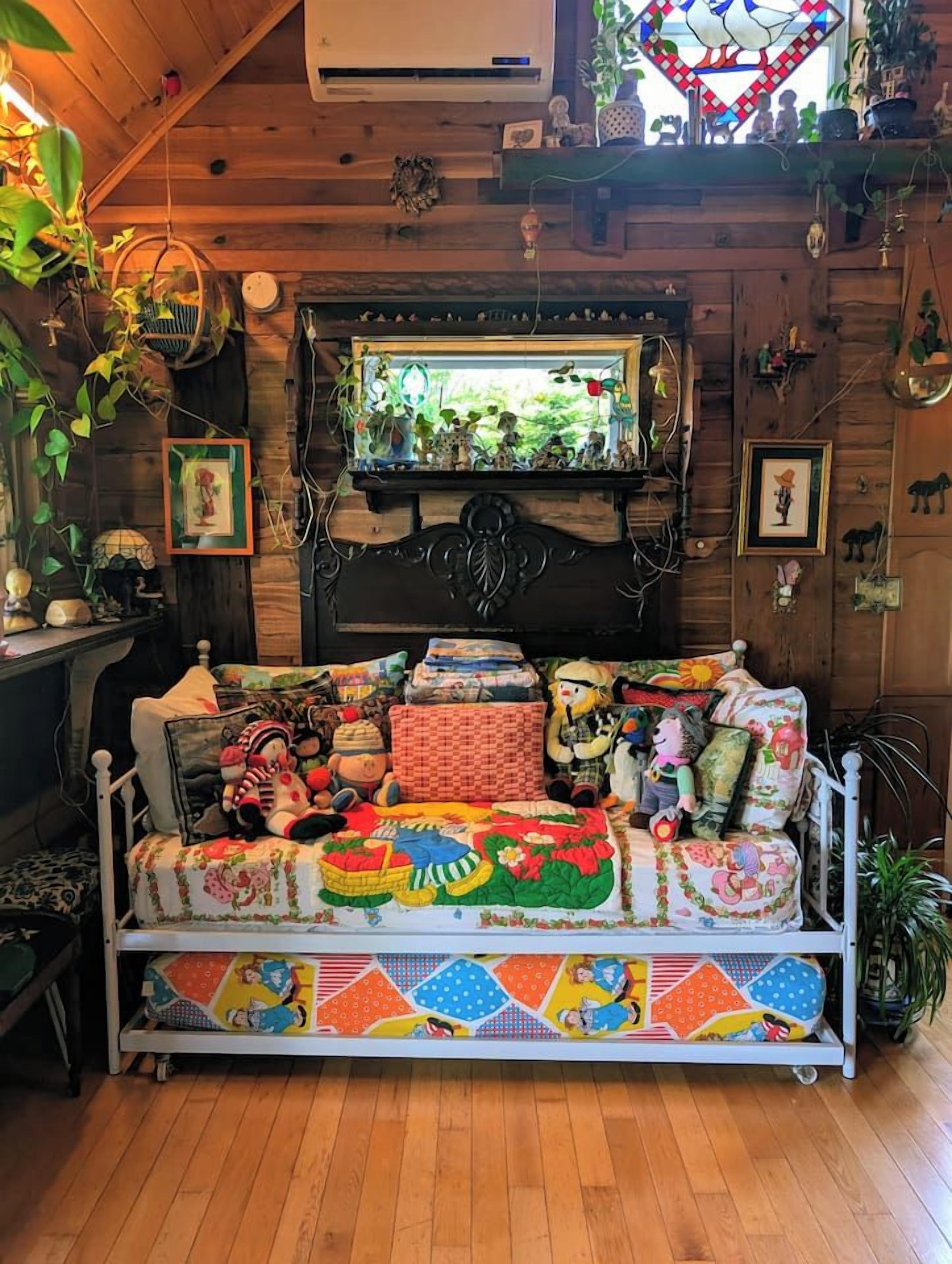 A cozy room with a wooden ceiling, a bed with colorful bedding, a stained glass window, and various wall decorations.