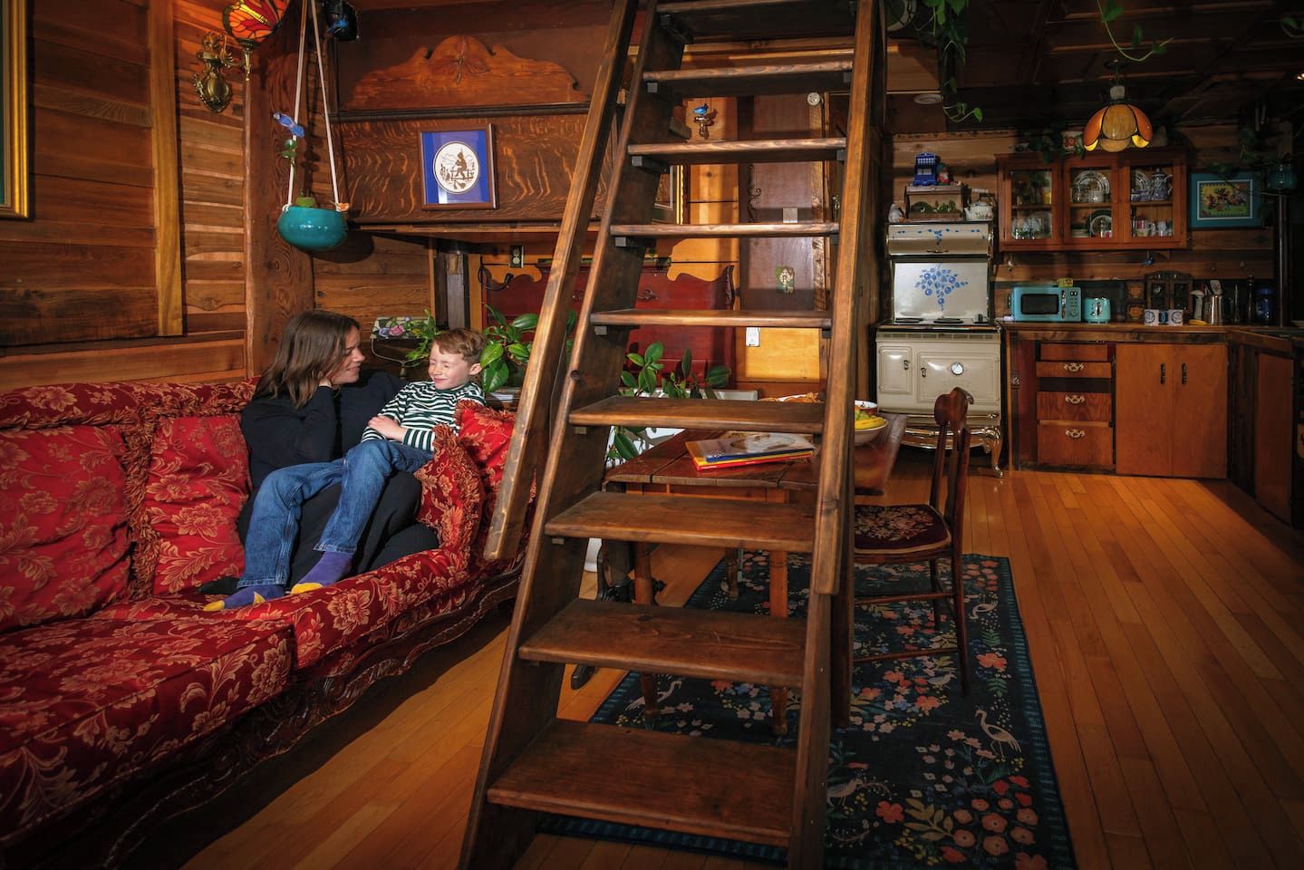 Un salon chaleureux avec un escalier en bois, un canapé rouge et un coin repas comprenant une table et des chaises en bois.