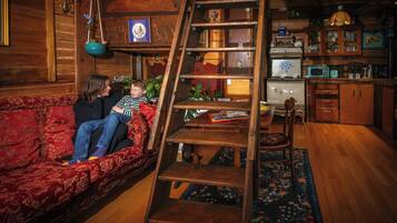 Un salon chaleureux avec un escalier en bois, un canapé rouge et un coin repas comprenant une table et des chaises en bois.