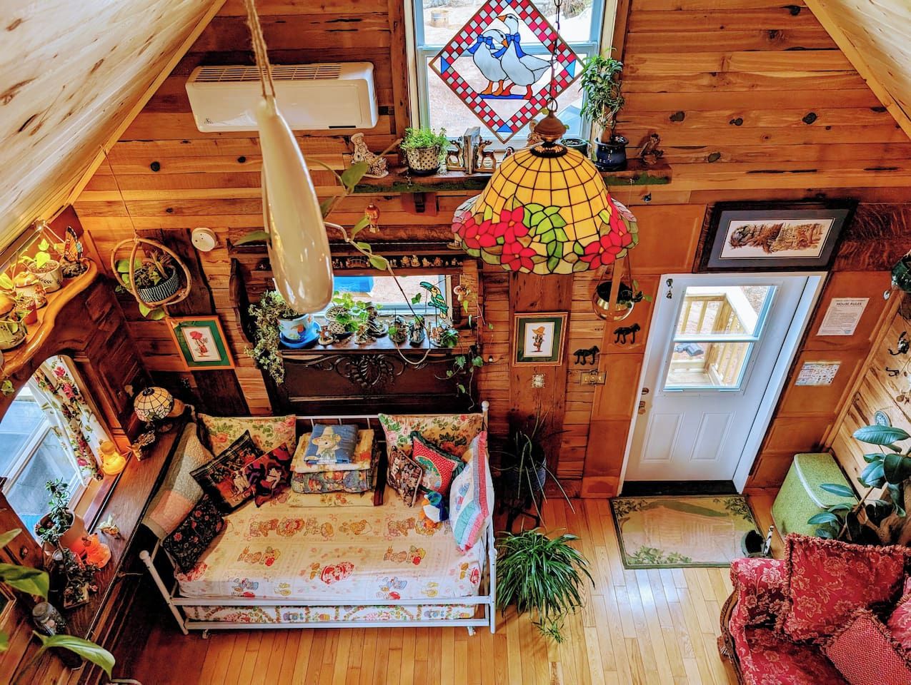 A cozy cabin interior with a bed, wooden walls, a hanging light fixture, and various decorations.