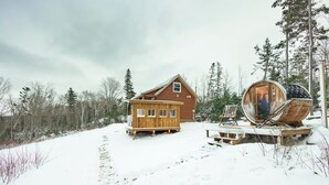 A wooden cabin with a large barrel sauna, surrounded by a snowy landscape and trees. - Miracles on Polly - Memory Lane Cabin (Belfast)