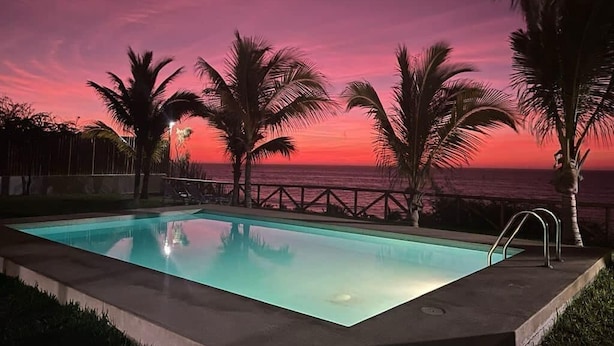 Una piscina con vista al océano al atardecer, rodeada de palmeras.