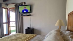 Habitación de hotel con cama, televisor en la pared, mesita de noche, lámpara y vistas al exterior.