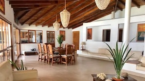 Amplia sala de estar con mesa de comedor, sillas, sofá y lámparas de mimbre colgantes.