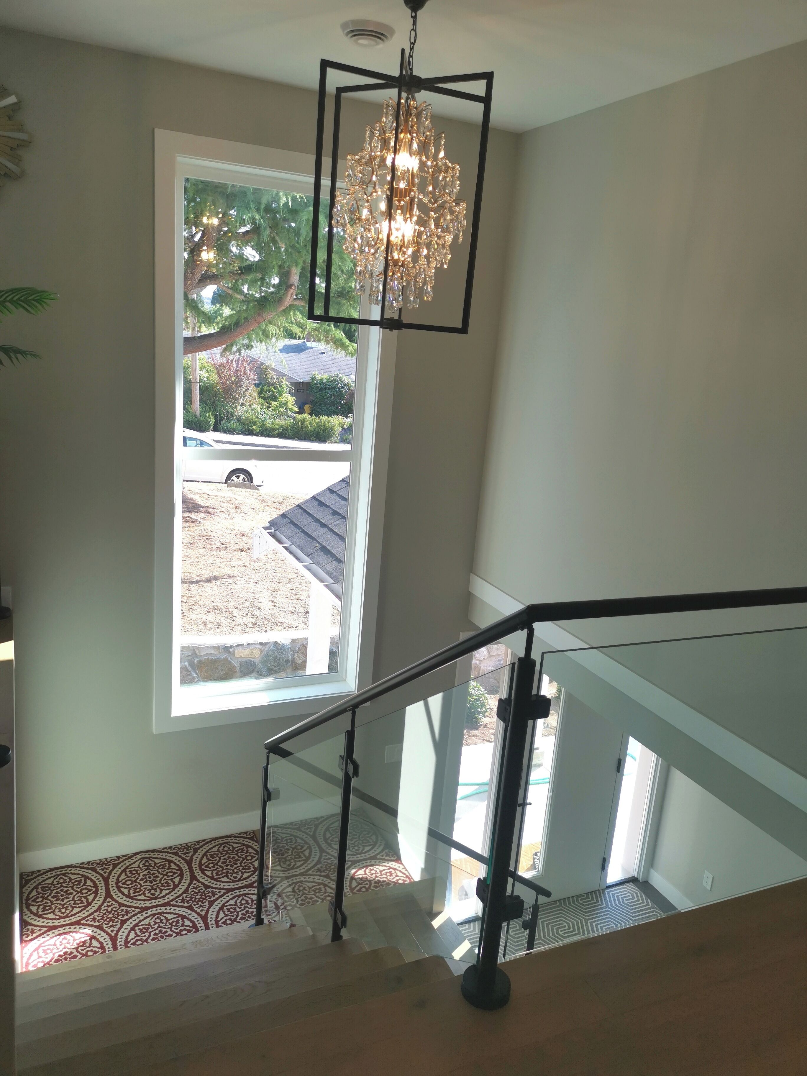 A staircase with a patterned carpet, a chandelier, and a view of a residential area outside.