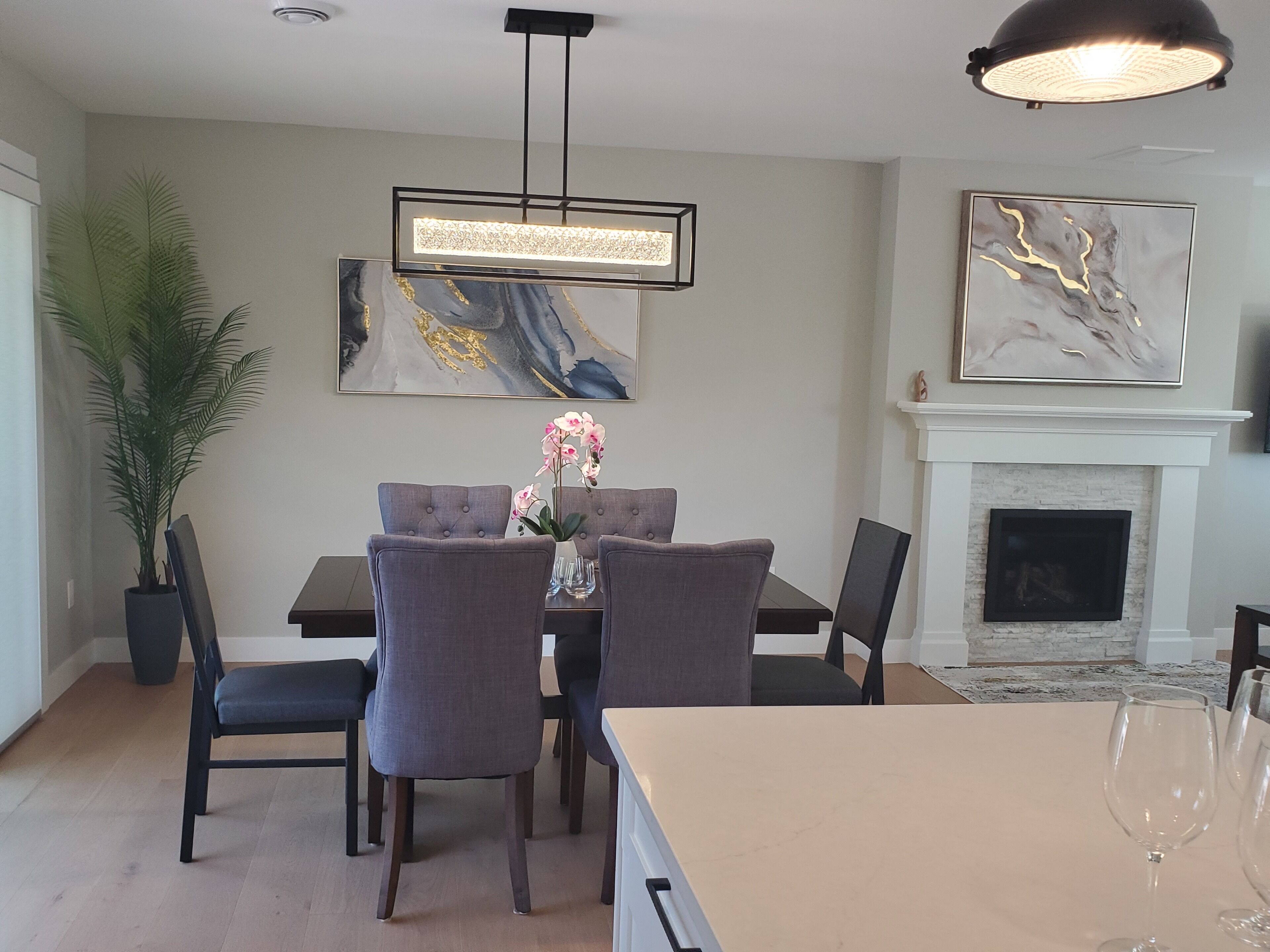 A dining area with a table set for four, surrounded by chairs, a potted plant, and a modern pendant light.